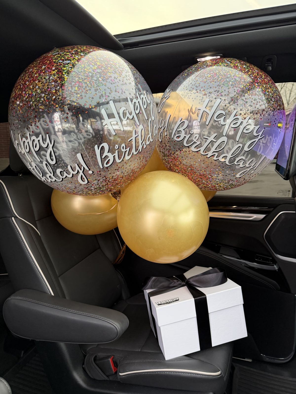 The rear cabin of a Cadillac Escalade ESV set up with balloons and a gift box before a celebration