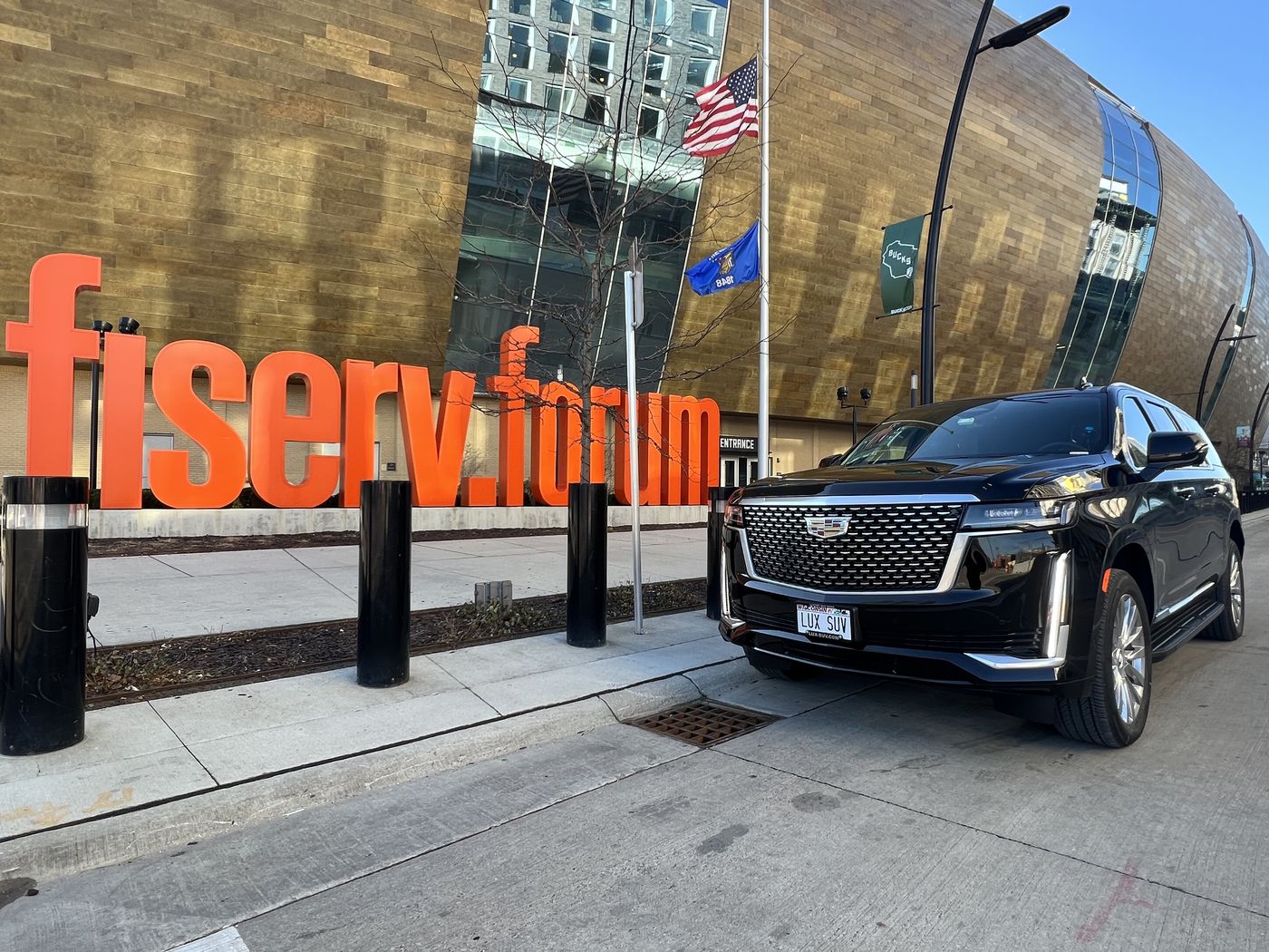 Black Cadillac Escalade ESV parked at the curb beside the orange Fiserv Forum lettering in Milwaukee
