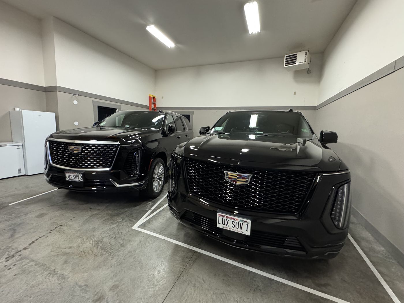 Two black Cadillac Escalade ESVs parked in the Luxury SUV Rides garage
