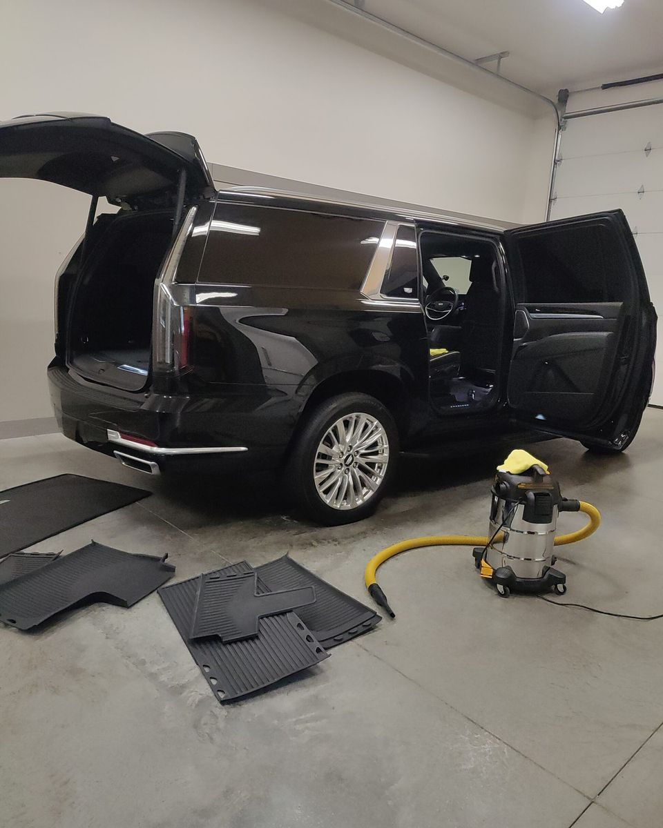 A Cadillac Escalade ESV with all doors open and floor mats out, being detailed in the garage