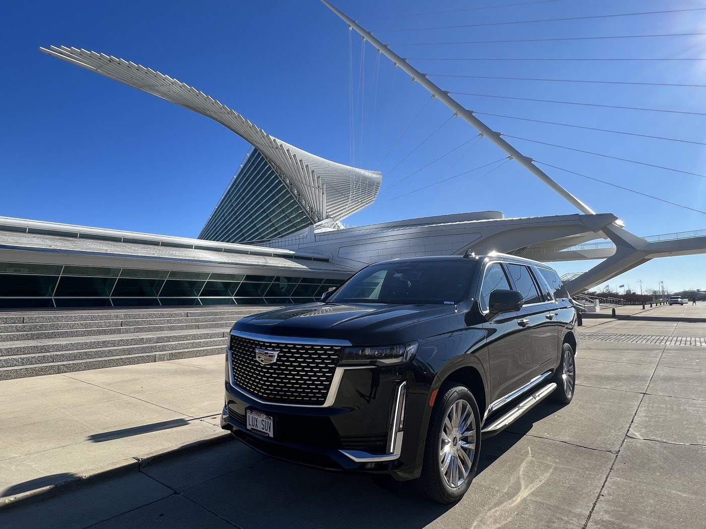 Black Cadillac Escalade ESV parked beside the Milwaukee Art Museum, with the white wings of the Quadracci Pavilion raised behind it