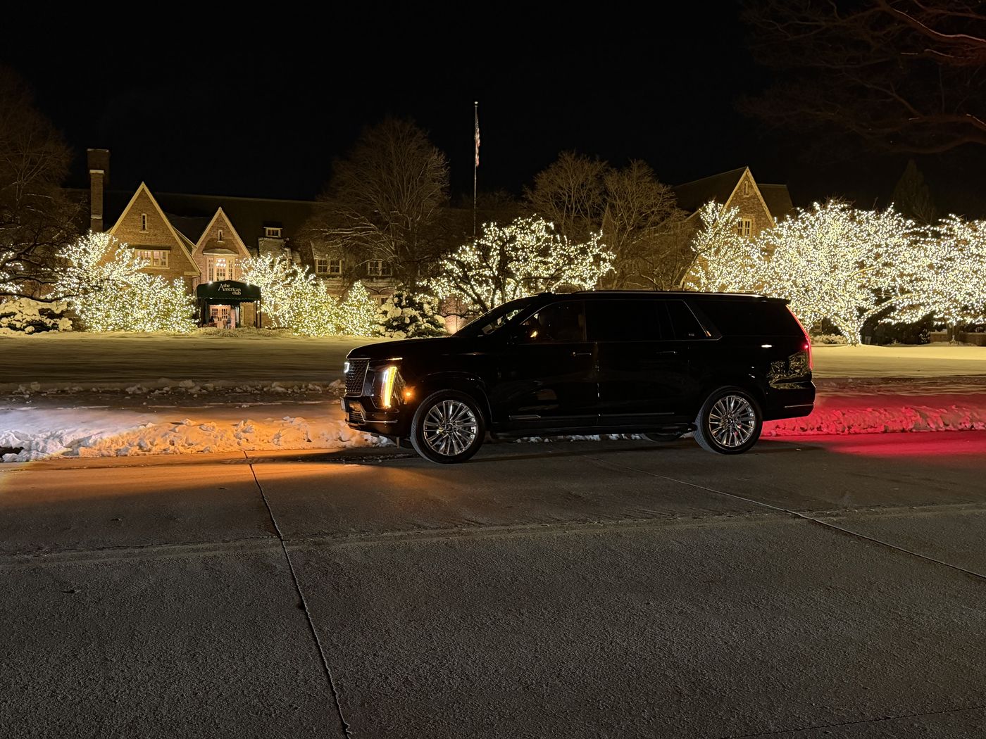 Black Cadillac Escalade ESV waiting outside The American Club on a winter night, snow on the ground and the trees lit for the holidays