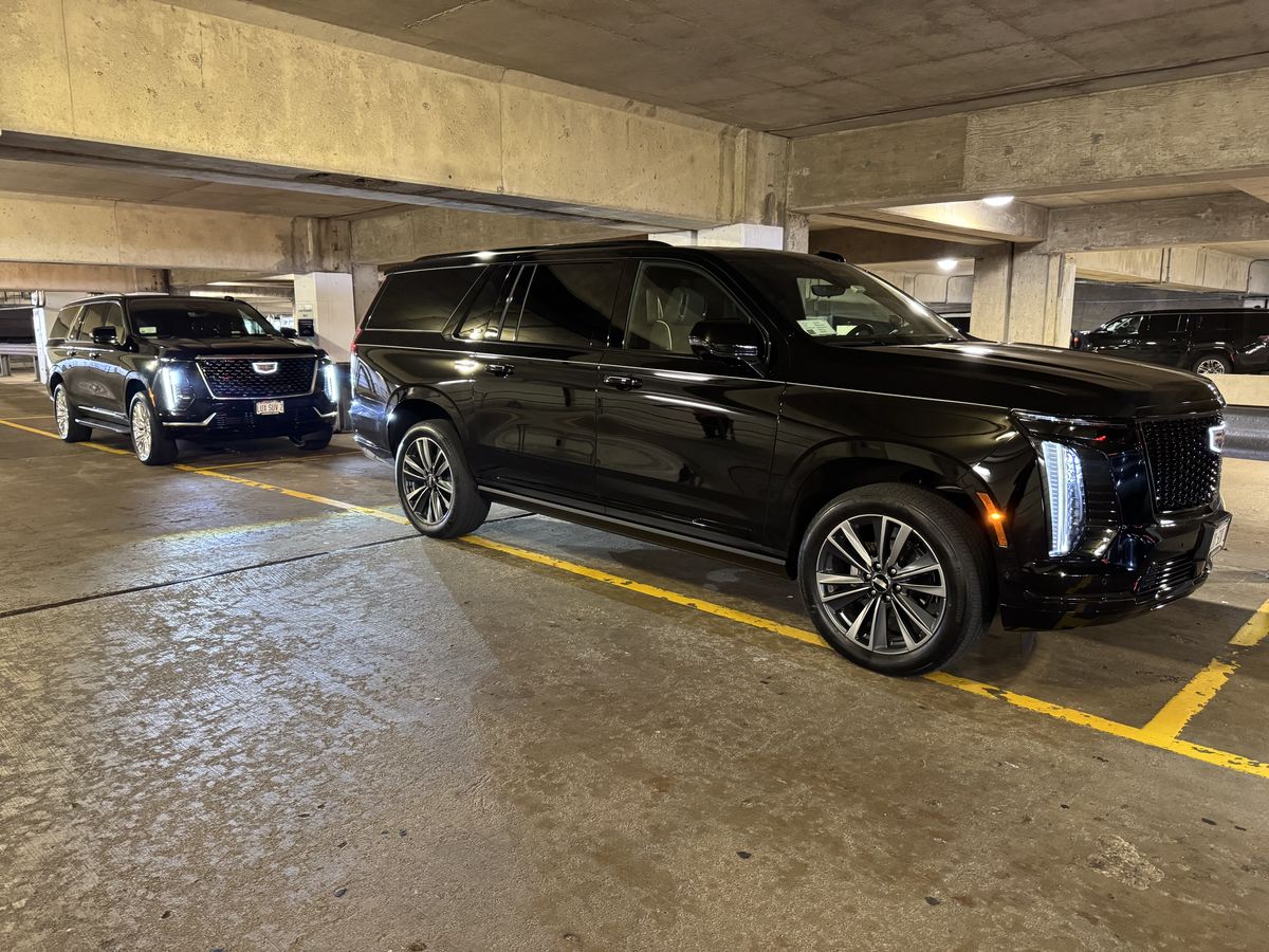 Two black Cadillac Escalade ESVs waiting in the ground level limo lane at Milwaukee Mitchell International Airport