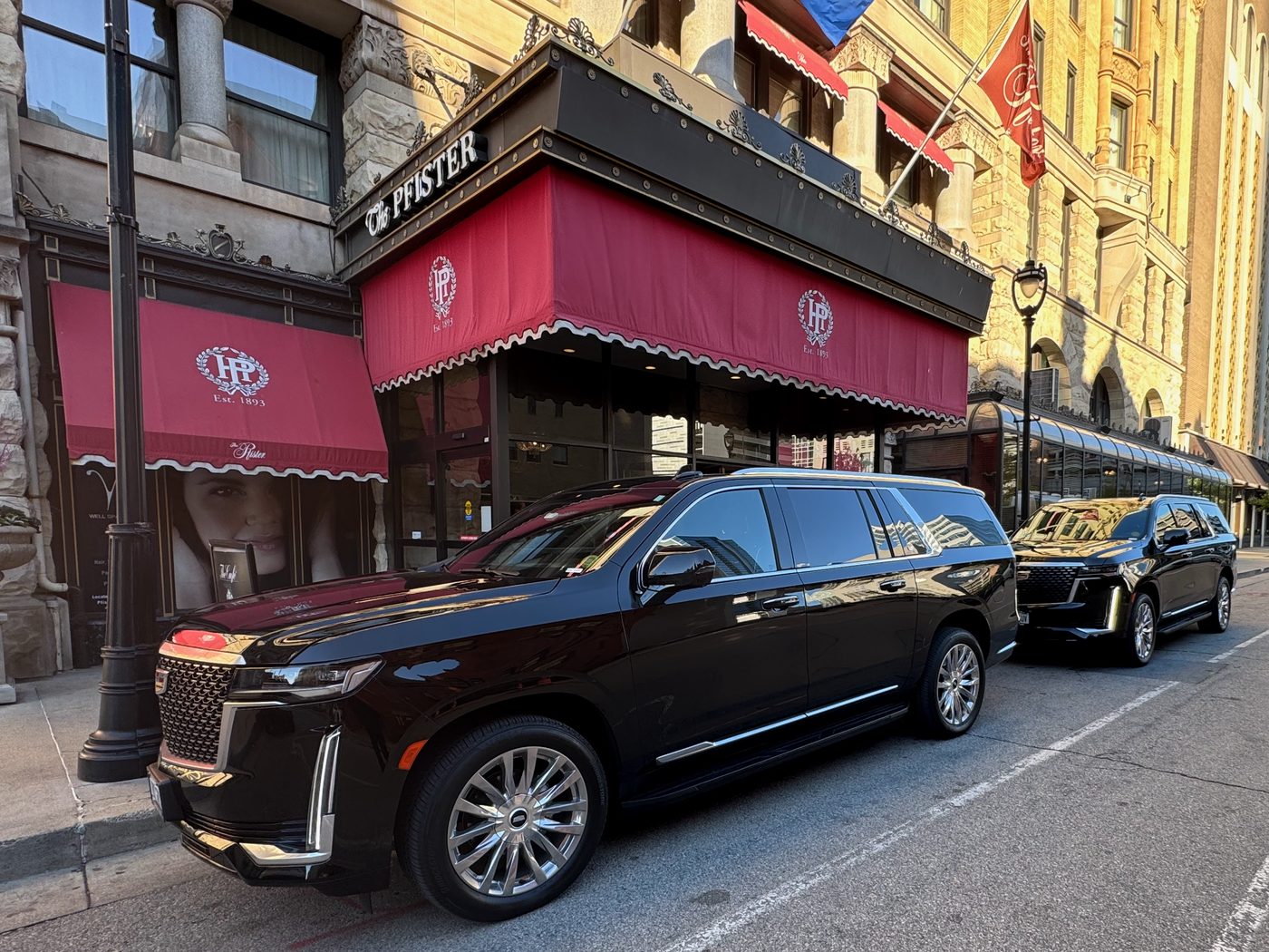 Two black Cadillac Escalade ESVs at the curb outside The Pfister Hotel in downtown Milwaukee in evening light