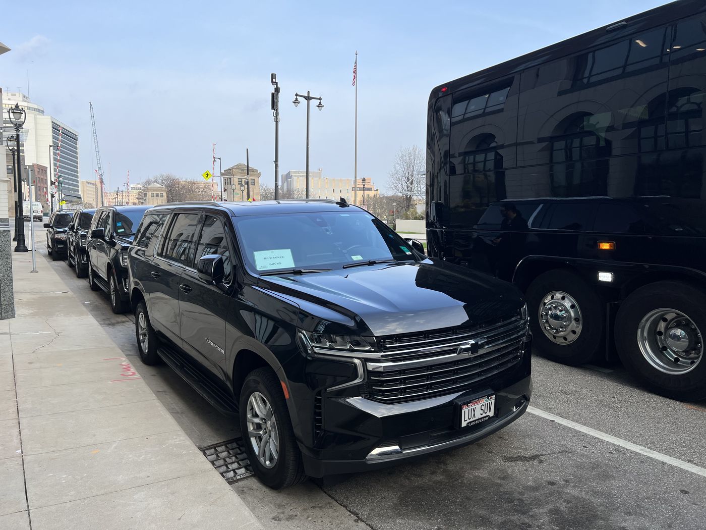 A line of black Chevrolet Suburbans staged at the curb behind the tour coaches