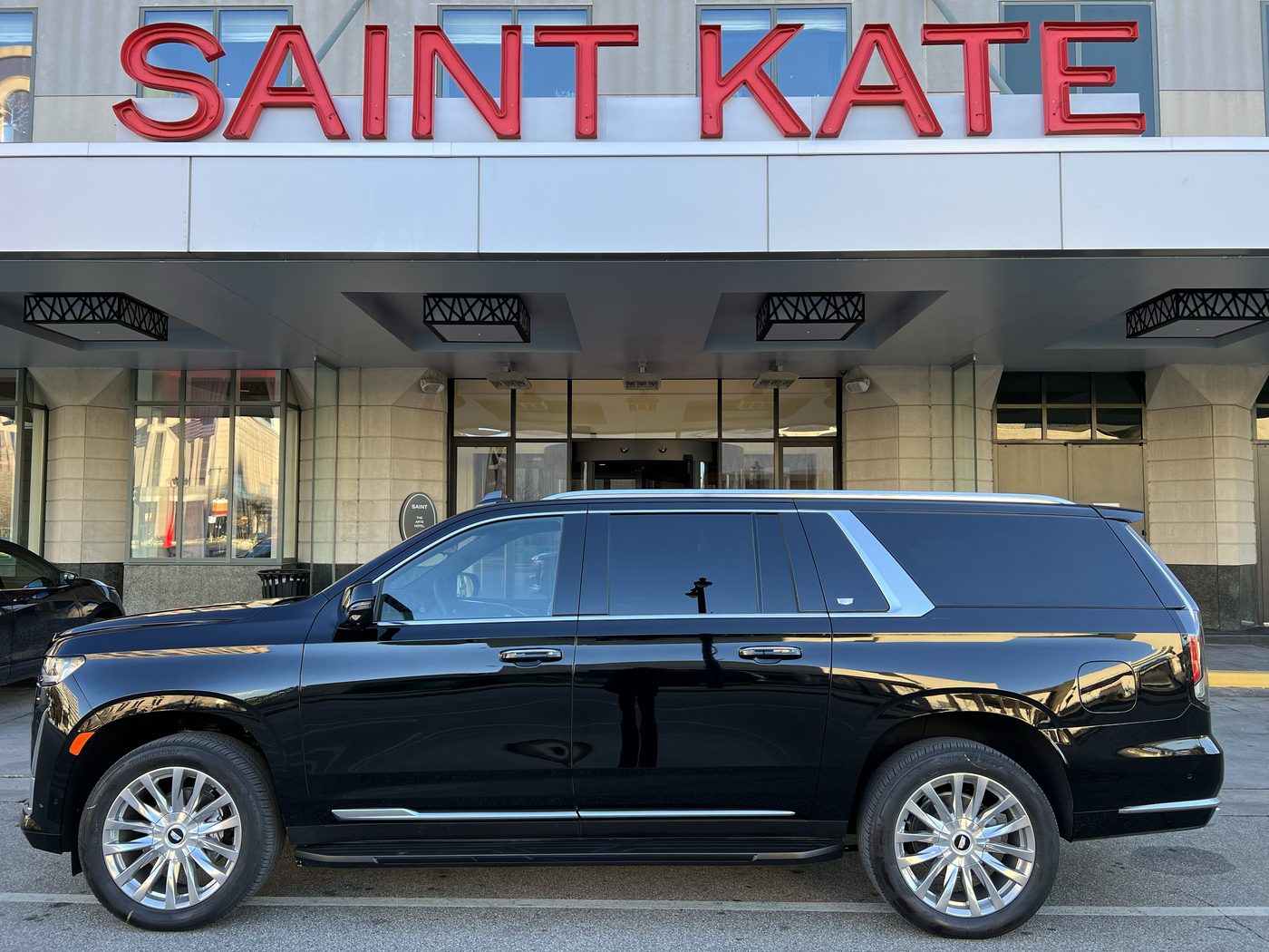 Black Cadillac Escalade ESV in full profile under the entrance canopy at Saint Kate, the Arts Hotel, in downtown Milwaukee, the hotel name in red above it