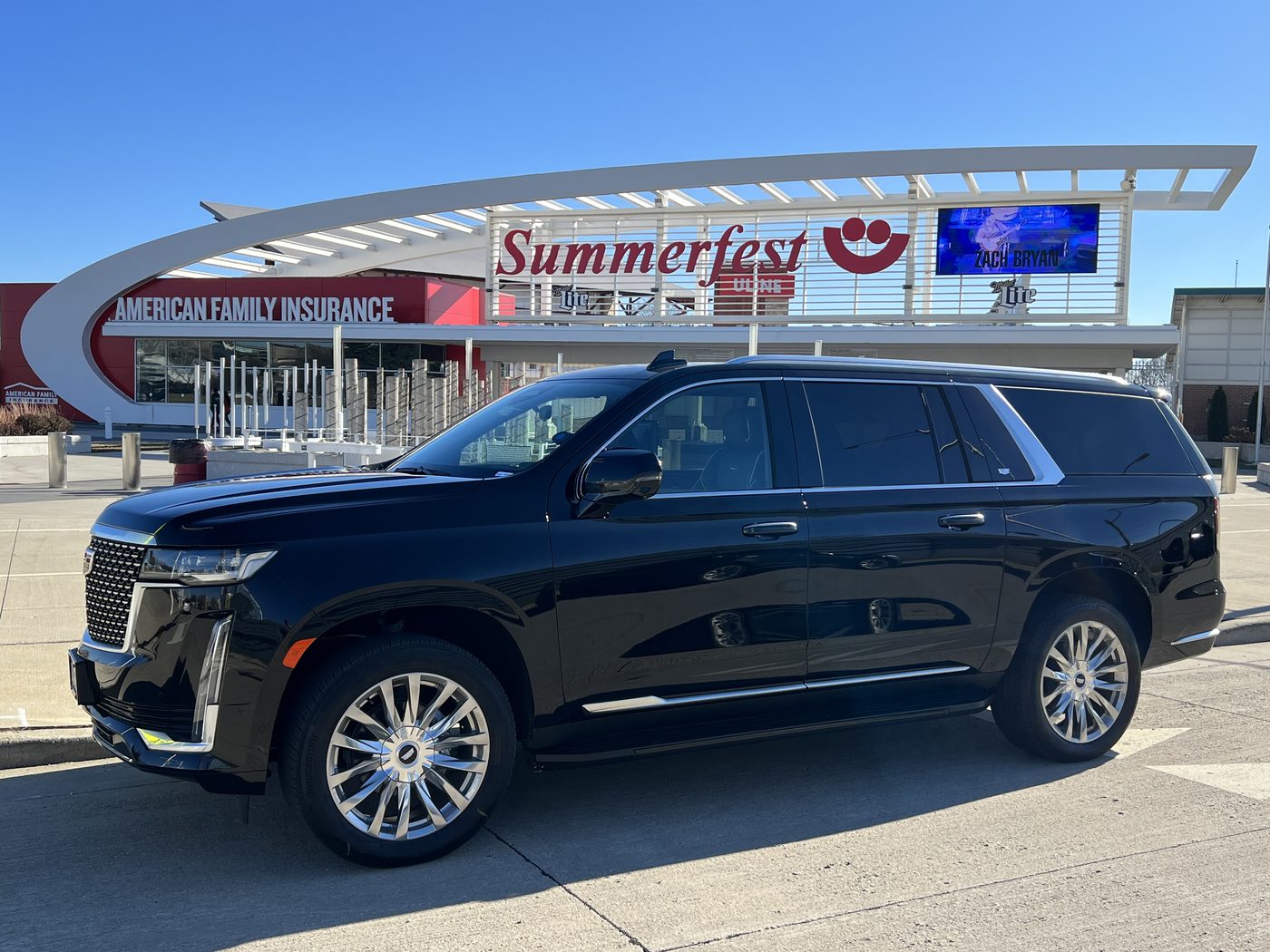 Black Cadillac Escalade ESV parked at the main Summerfest gate on the lakefront, the American Family Insurance Amphitheater behind it