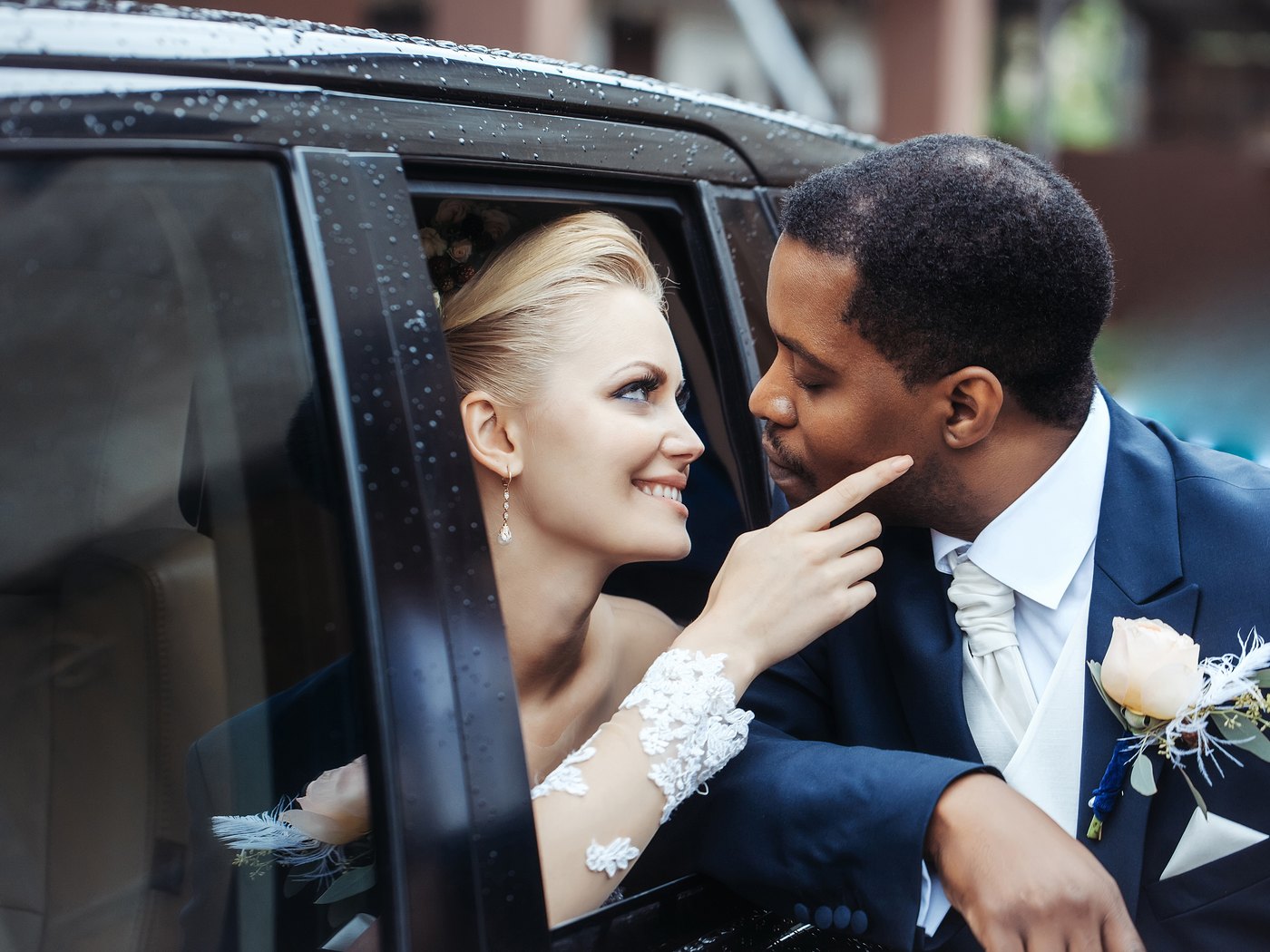 A bride and groom at the open door of a black SUV on a wet morning