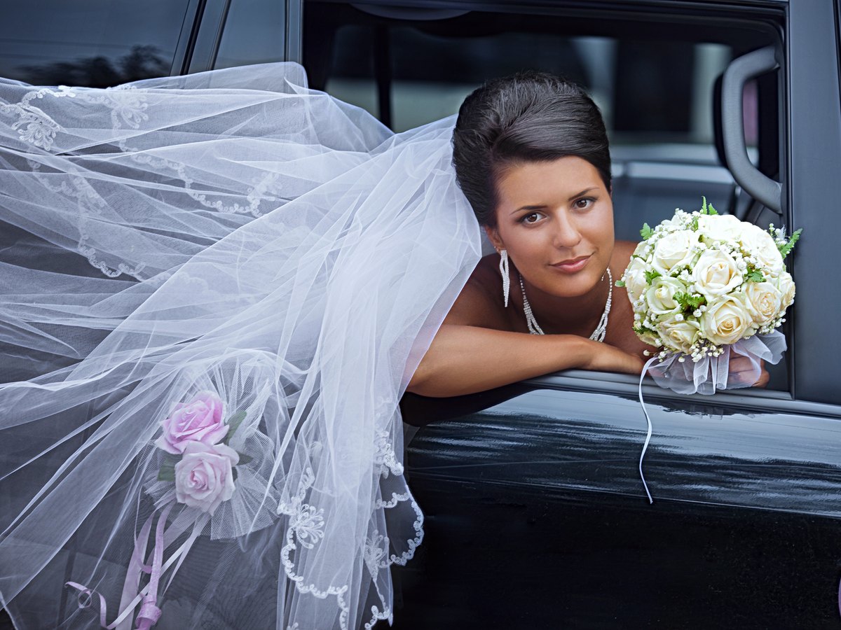A bride leaning from an open car door, her veil spilling across the vehicle